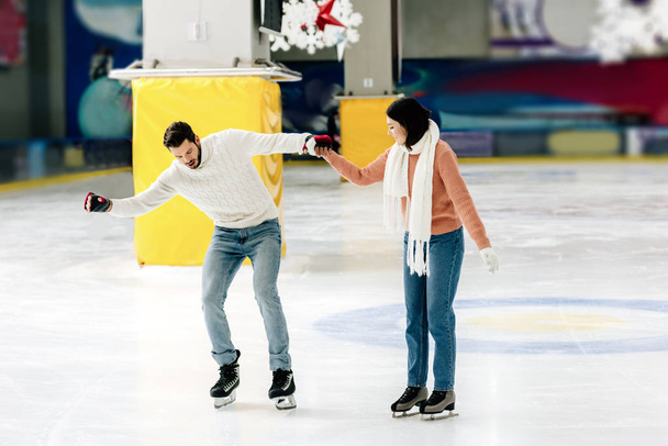 beautiful young woman teaching man to skate on a rink and holding hands - Photo, Image