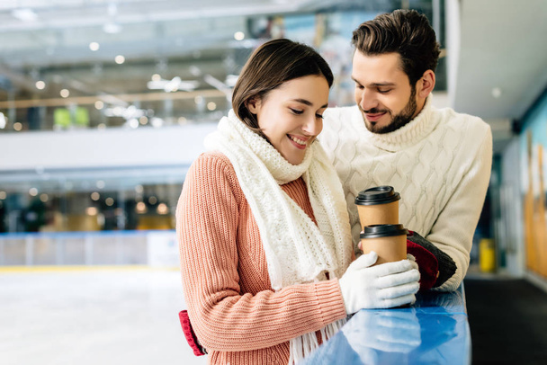 Güzel mutlu çift ellerinde kahve ile buz pateni pistine gidiyorlar. - Fotoğraf, Görsel