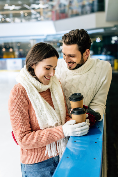 hermosa pareja positiva sosteniendo café para ir en pista de patinaje
 - Foto, Imagen