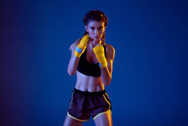 Fit caucasian woman in sportswear boxing on blue studio background in neon light - Photo, Image