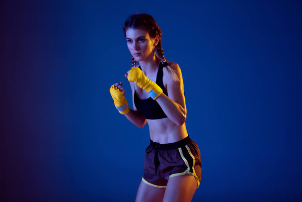 Fit caucasian woman in sportswear boxing on blue studio background in neon light - Photo, Image