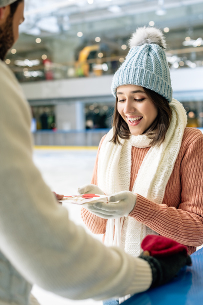 man giving greeting card on valentines day to happy woman on skating rink - Photo, Image