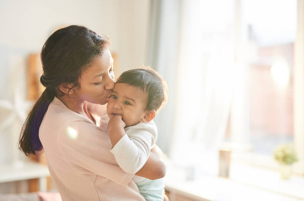 Молодая мать держит ребенка на руках и целуется дома
 - Фото, изображение