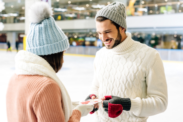 smiling man giving greeting card on valentines day to woman on skating rink - Zdjęcie, obraz