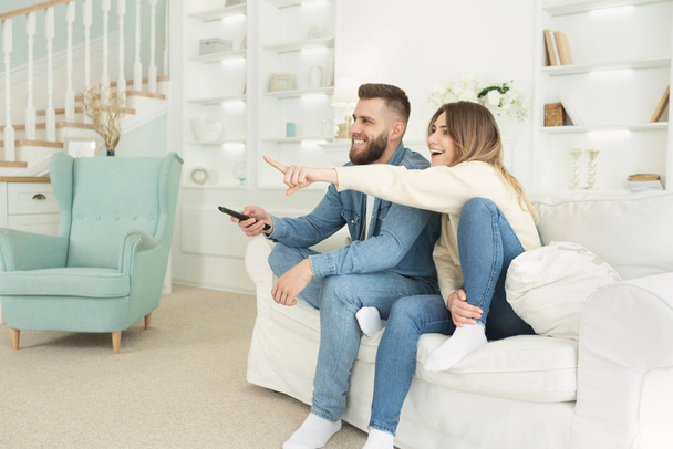 junge Ehepartner fernsehen, aufgeregte Frau zeigt auf Bildschirm - Foto, Bild