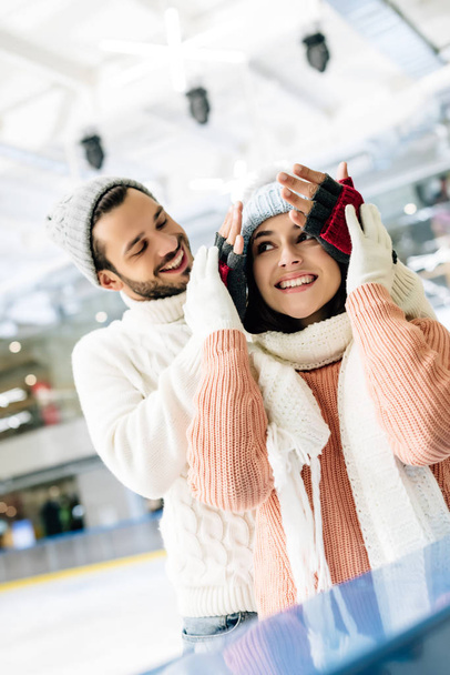 smiling man closing eyes to happy girl to make a surprise on skating rink - Photo, Image