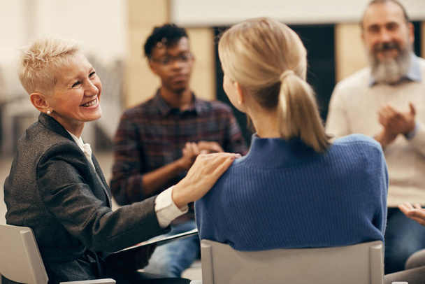 Lächelnde reife Frau mit kurzen Haaren im Gespräch mit der jungen Frau während der Therapiestunde - Foto, Bild