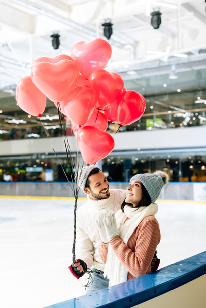όμορφο ζευγάρι με κόκκινα μπαλόνια σχήμα καρδιάς ξοδεύουν χρόνο για πατινάζ παγοδρόμιο την ημέρα του Αγίου Βαλεντίνου - Φωτογραφία, εικόνα
