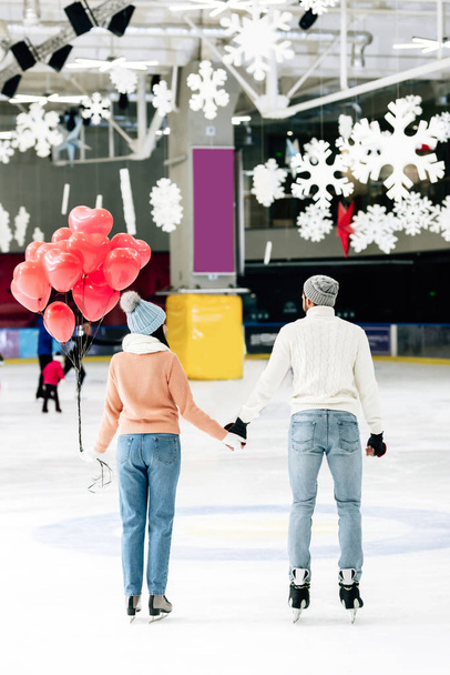 back view of couple with red heart shaped balloons holding hands on skating rink on valentines day - Photo, Image