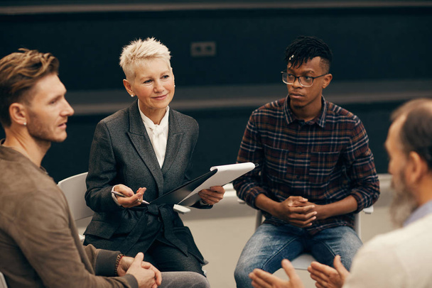 Ομάδα επιχειρηματιών που κάθονται και συζητούν τα μελλοντικά σχέδια με ώριμη γυναίκα κατά τη διάρκεια της συνάντησης - Φωτογραφία, εικόνα