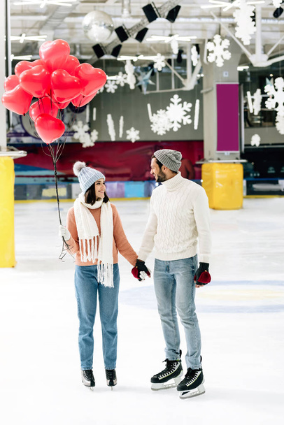 pareja alegre con globos rojos en forma de corazón tomados de la mano en la pista de patinaje en el día de San Valentín
 - Foto, Imagen