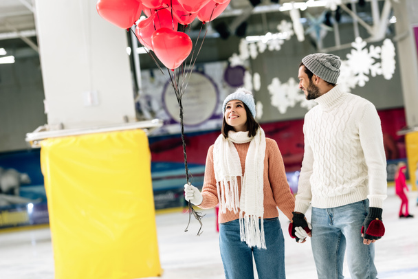 cheerful couple with red heart shaped balloons spending time on skating rink on valentines day - Photo, Image
