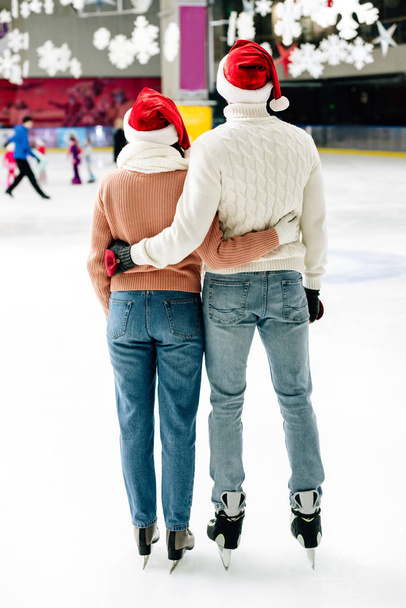 vista posteriore della coppia felice in cappelli di Babbo Natale che abbraccia sulla pista di pattinaggio
 - Foto, immagini