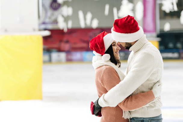 Noel Baba şapkalı güzel bir çift buz pateni pistinde vakit geçiriyor. - Fotoğraf, Görsel