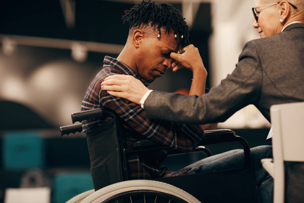 アフリカの若い障害者の男性は車椅子に座って、女性が支援する病気を心配しました - 写真・画像