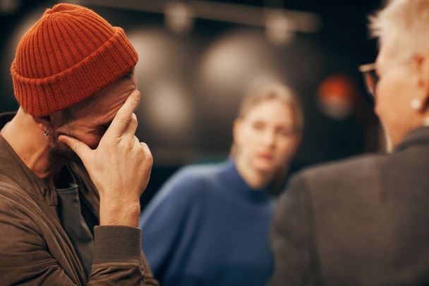 Jonge droevige man in hoed bezorgd over problemen en het bezoeken van de lessen wanneer mensen elkaar steunen en vertellen problemen - Foto, afbeelding