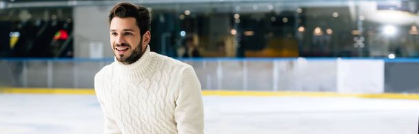 plano panorámico de hombre guapo sonriente en jeans y suéter patinaje sobre pista
 - Foto, imagen