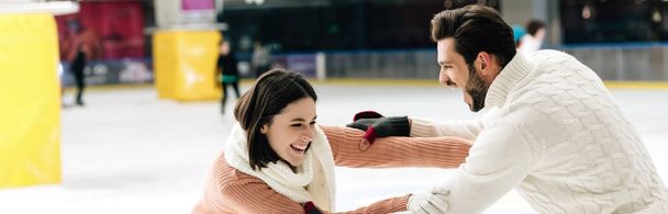 panoramisch schot van vrolijk jong paar hebben plezier op schaatsbaan   - Foto, afbeelding