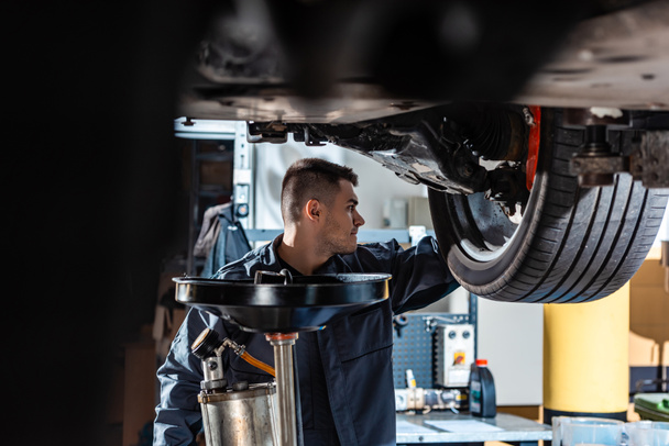 selective focus of mechanic standing under raised car near waste oil extractor - Photo, Image