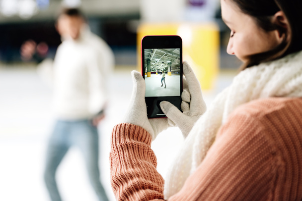 selective focus of beautiful woman taking photo of man on smartphone on skating rink - Photo, Image