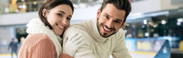 panoramic shot of cheerful couple in sweaters spending time on skating rink   - 写真・画像