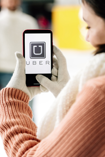 KYIV, UKRAINE - NOVEMBER 15, 2019: cropped view of woman in gloves holding smartphone with UBER app on screen - 写真・画像