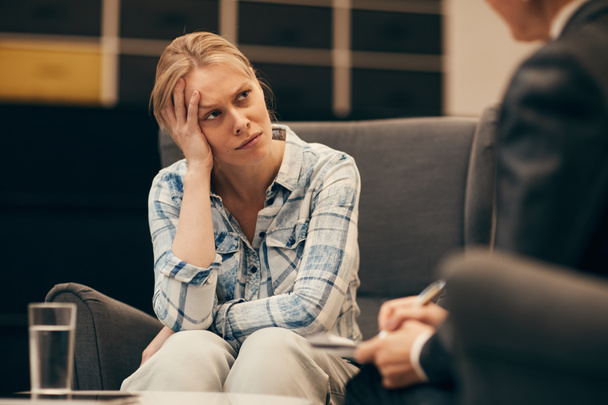 Молодая женщина с депрессией сидит на диване и разговаривает с психологом в офисе
 - Фото, изображение