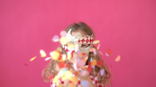Fancy girl blowing confetti against pink bakground. Happy child having fun at carnival. Mardi gras holiday concept - Video