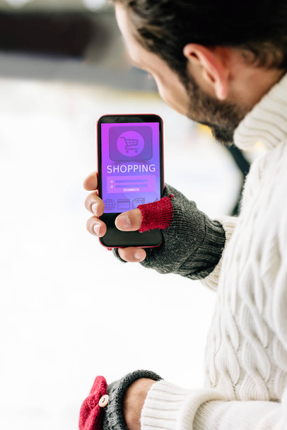 KYIV, UKRAINE - NOVEMBER 15, 2019: cropped view of man in gloves holding smartphone with shopping app on screen, on skating rink - 写真・画像
