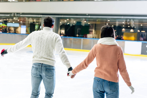 back view of young couple holding hands on skating rink  - 写真・画像