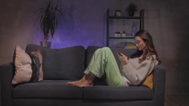 Young mother and son sitting on the couch in a cozy room and playing on the phone - Materiał filmowy, wideo