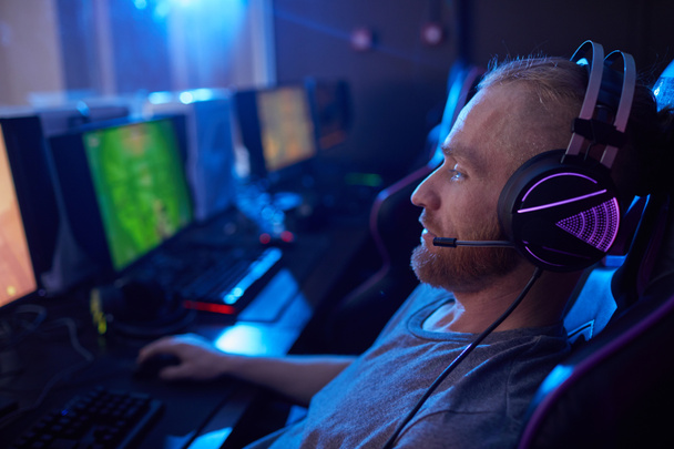 バックライト付きゲームヘッドフォンでの若い男のサイドビュー暗いコンピュータクラスのコンピュータゲームで座って演奏 - 写真・画像