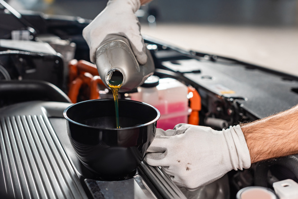 обрезанный вид механика, заливающего масло в двигатель автомобиля
 - Фото, изображение