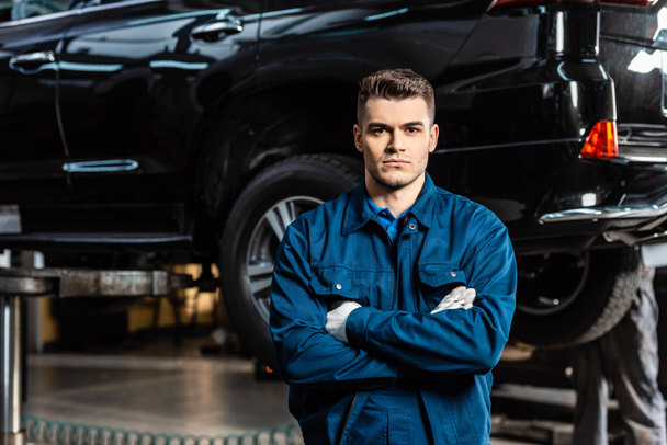 handsome, serious mechanic standing with crossed arms and looking at camera - Φωτογραφία, εικόνα