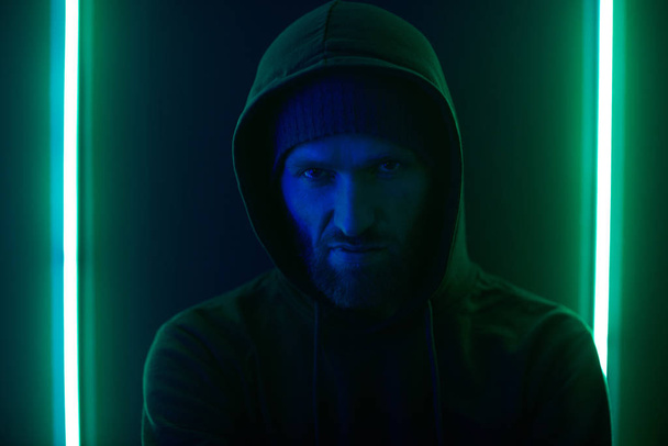 Portrait of bearded gangster wearing hoody looking angry while standing against the wall - Foto, Bild