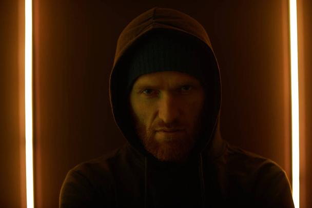 Portrait of bearded gangster wearing hoody looking angry while standing against the wall - Foto, afbeelding