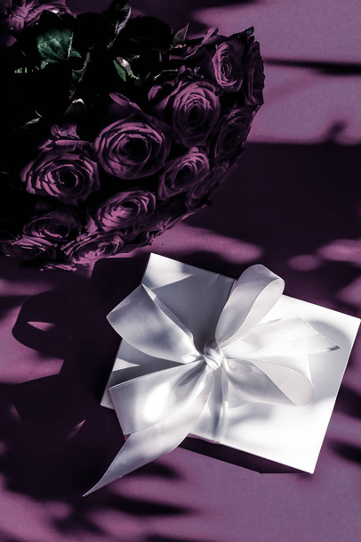 Πολυτελείς διακοπές μεταξωτό κουτί δώρου και μπουκέτο τριαντάφυλλα σε μωβ πλάτη - Φωτογραφία, εικόνα