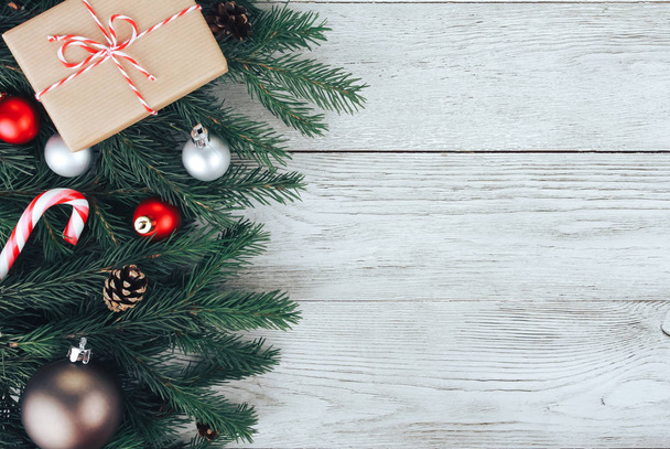 Концепция Рождества. Красные рождественские безделушки, елки, зеленая подарочная коробка, конфетная трость, конусы на белом деревянном столе. Новый год, зимние каникулы, копировальное пространство, вид сверху
 - Фото, изображение