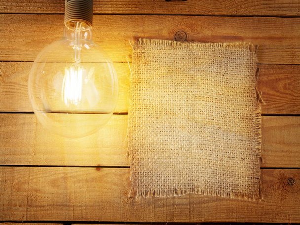 Kousek starého plátna. Visící žárovka na dřevěné stěně. Žárovka typu Edison. Mezera pro text. - Fotografie, Obrázek