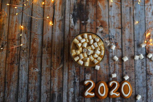Номер 2020 от пряников cookies.cocoa, зефир, домашнее печенье и сердце из кофейных зерен на деревянном фоне с боке новогодние огни
. - Фото, изображение
