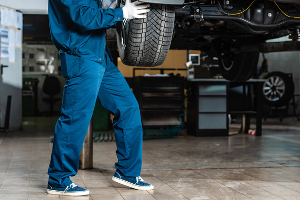 cropped view of mechanic installing wheel on raised car in workshop - Photo, Image