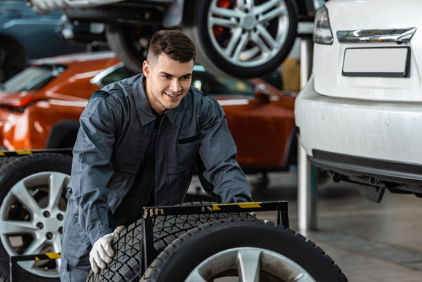 handsome, smiling mechanic holding new tire in workshop - Photo, Image