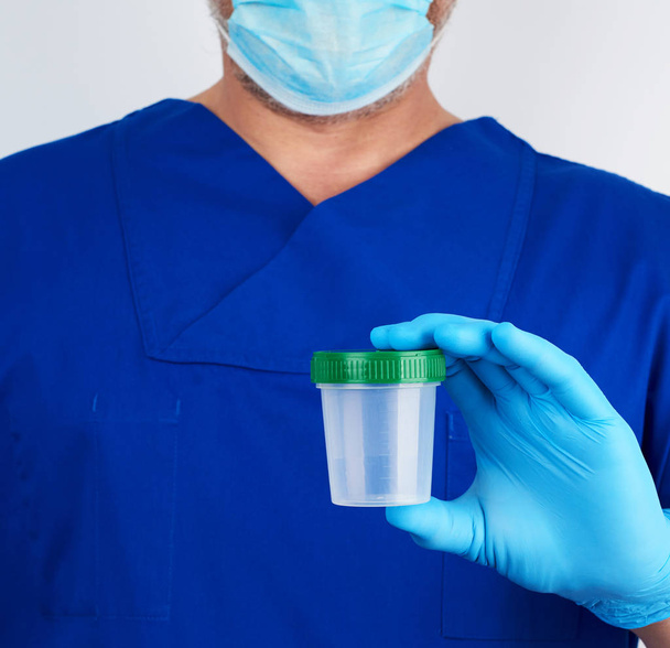 doctor in blue uniform and latex gloves is holding an empty plas - Фото, зображення
