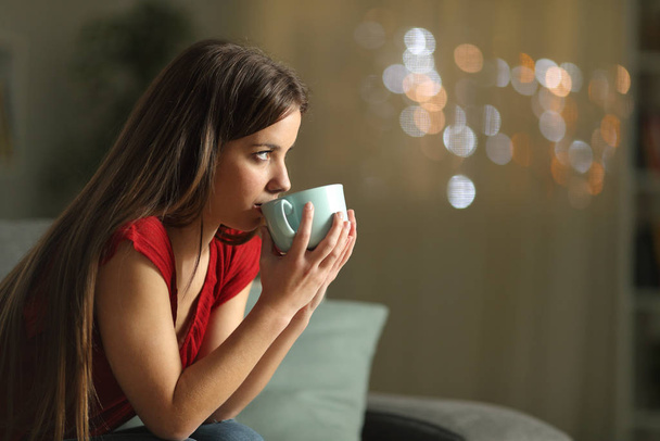 Woman looking away drinking coffee in the night - Фото, изображение