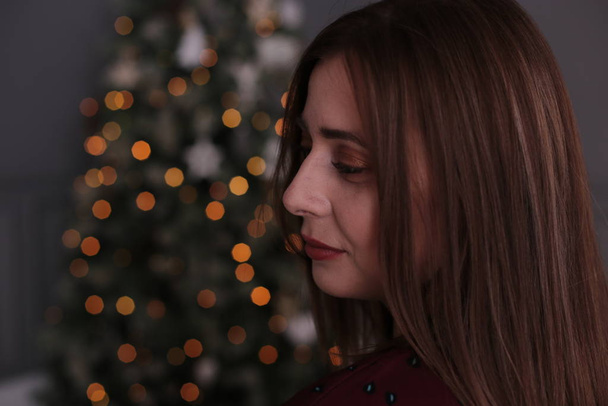 Menina bonita com cabelo escuro curto com uma grinalda perto de uma árvore de Natal decorada
 - Foto, Imagem