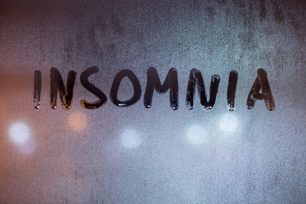 Слово "омния" написано на ночном мокром оконном стекле крупным планом на размытом фоне - Фото, изображение