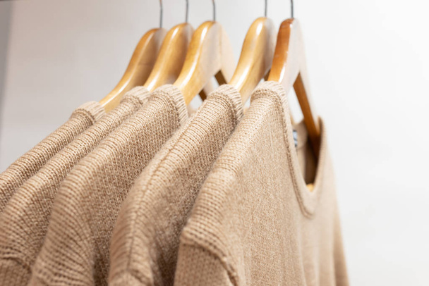 Suéteres cálidos de lana de color beige colgando de perchas
 - Foto, imagen