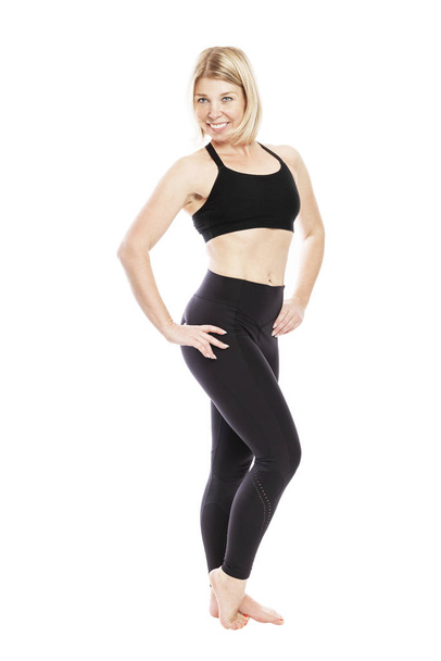 A young smiling woman in black sportswear is standing full length. Isolated over white background.  - Foto, imagen