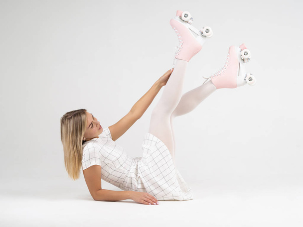 Joyful jonge vrouw met quad rolschaatsen schoenen liggend op de vloer met opgeheven benen op een witte achtergrond - Foto, afbeelding