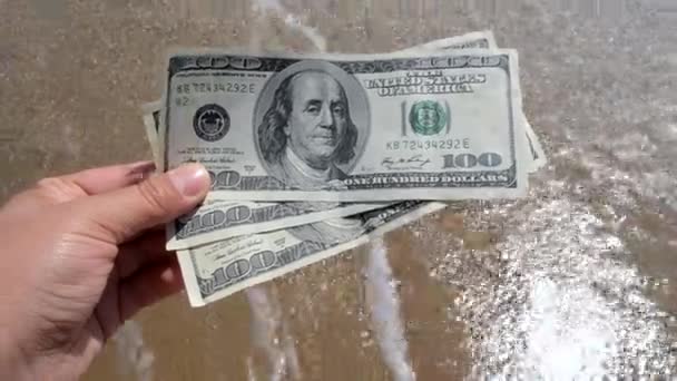 Chica sosteniendo una cuenta de dinero de 300 dólares en el fondo de las olas del mar - Metraje, vídeo